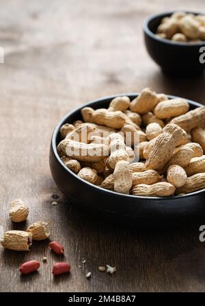 unpeeled peanuts in a black bowl on a dark wooden  background. Macro and close up image. Stock Photo