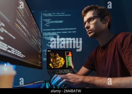 Closeup portrait of handsome IT support specialist monitoring feedback and complaints of online application users, sitting at big pc screen, typing, wearing glasses and red t-shirt Stock Photo