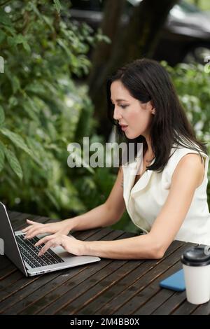 Young female entrepreneur working on laptop in outdoor cafe Stock Photo