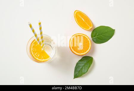 A glass of mineral water and a slice of orange on a light  table with fresh juicy fruit oranges and green leaves. Summer time. Top view image Stock Photo