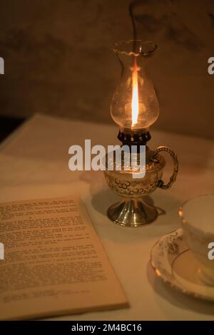 photo of a lit kerosene lamp standing side by side on a table with an open book and an empty cup on a saucer cup Stock Photo