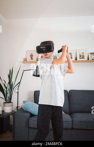 Boy child playing swordplay video games at home, wearing virtual reality vr headset and holding remote controller Stock Photo