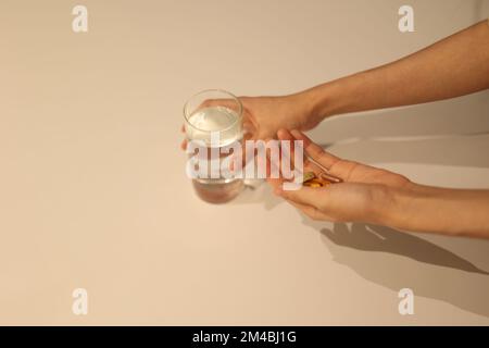 Woman is taking medicine with cup of water on the white table, girl is taking nutritional supplement by hand Stock Photo