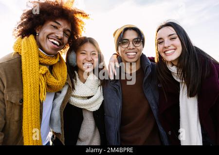 Portrait of four multiracial student friends in winter clothes smiling at camera Stock Photo