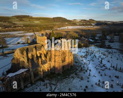 Aerial shot of Melrose Abbey with a layer of snow and frost at sunset on a crisp winter day in December. Stock Photo