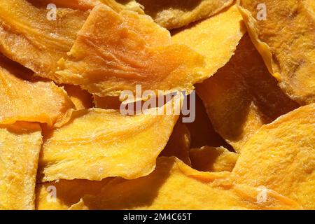 Dried mango slices close-up on a white. Top view. Closeup. Mango chips background. Dehydrated crispy fruit slices, pieces. Heap of sun-dried yellow fr Stock Photo