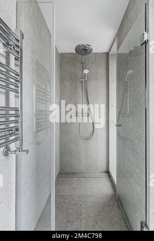 Shower cabin with stone cladding on walls and floors, glass door with chrome hinges and heated towel rail Stock Photo