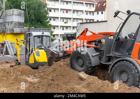 Small loader and excavator digger machine moving heap of earth and debris rubble at construction site. New building scaffold and engineering equipment Stock Photo