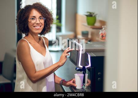 Company employee making herself a drink in the office kitchen Stock Photo