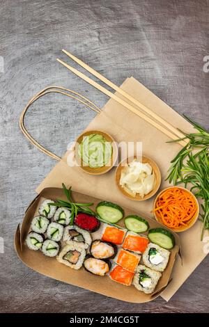Takeaway food. Sushi and sliced cucumbers in paper plates. Seasonings in bowls. Paper bag. Flat lay. Brown background. Stock Photo