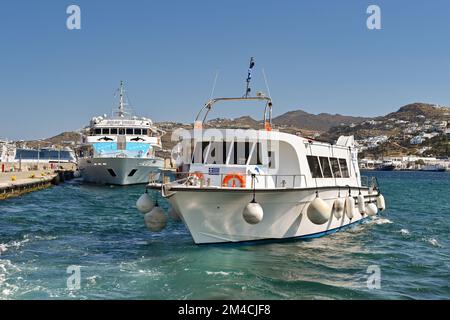 Mykonos, Greece - June 2022: Small ferry boat arriving in the town's harbour with a large ferry in the background Stock Photo