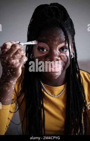 Smiling black woman with vitiligo doing makeup with brush Stock Photo