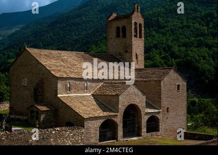This Pyrenean church, built in the 1500s, has a fortified bell tower that may be up to 300 years older: the Iglesia de San Miguel or Church of St Michael, under a fine roof of ragged fish scale pizarra stone slates, at Linás de Broto, Torla-Ordesa, Huesca, Aragon, Spain. Stock Photo