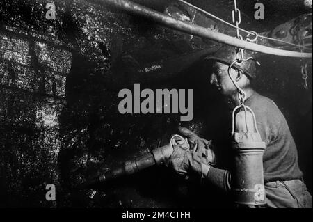 Coal miner / hewer working underground in shaft, extracting coal by hand with pneumatic hammer / pick in colliery / coal mine / coal pit Stock Photo