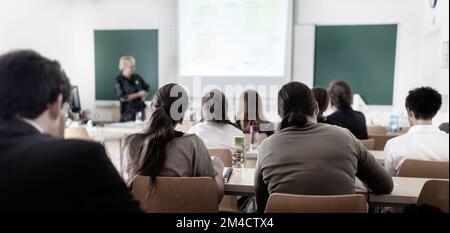 Teacher at university in front of a whiteboard screen. Students listening to lecture and making notes. Stock Photo