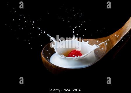 fresh raspberry splashing milk on a wooden spoon, splash effect with black background Stock Photo