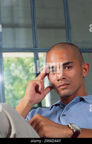 young man pausing while reading to look at the camera with his hand up to his head in a pensive mood Stock Photo