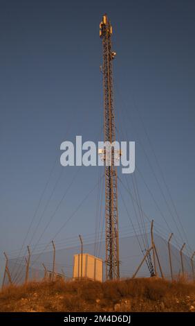 Isolated cell tower surrounded by barbed wire fence Stock Photo