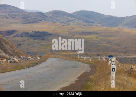A bent asphalt road against the backdrop of a curved dirt path going up the hill Stock Photo