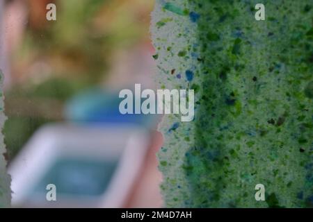 Sheet of recycled paper drying on a glass window and two plastic basin full of paper pulp in the background. Stock Photo