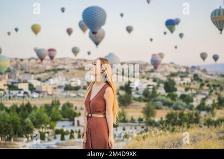 Tourist woman looking at hot air balloons in Cappadocia, Turkey. Happy Travel in Turkey concept. Woman on a mountain top enjoying wonderful view Stock Photo