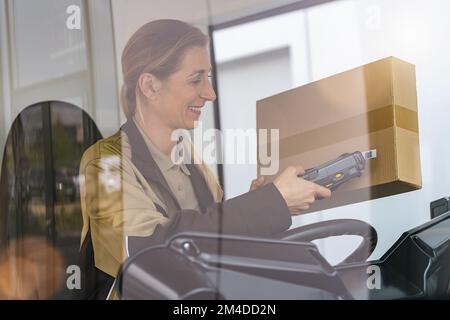 Delivery driver using barcode scanner checking pacel in a van outside a warehouse Stock Photo