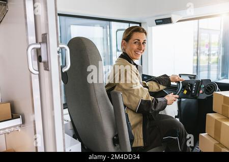 Delivery woman driving van with packages on the front seat. Happy female courier in truck. Portrait of confident express courier driving his delivery Stock Photo