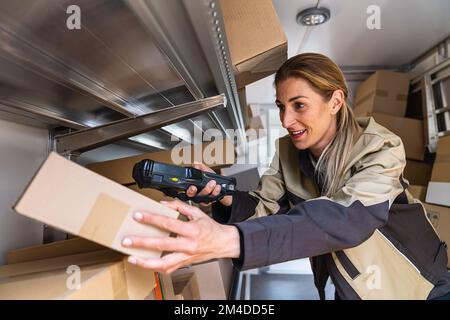 happy female delivery agent scanning barcode inside her van on a parcel. Courier Delivery concept image Stock Photo