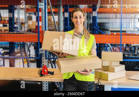smiling female worker holding packing cases after sealing it with adhesive tape at warehouse of freight forwarding company Stock Photo