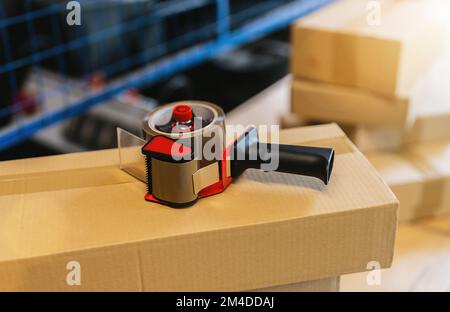 shipping boxes with tape dispenser and adhesive tape at warehouse of freight forwarding company Stock Photo