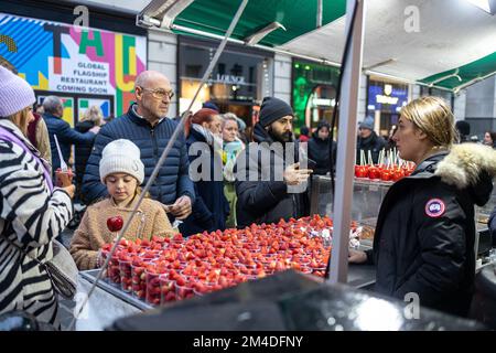 London, UK - December 2022, The girl chose apples in red icing. A vendor selling strawberries in cups at Covent Garden Stock Photo