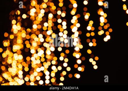 Festive bright blurred golden background. On Christmas black curtain, yellow bokeh lights are shining out of focus. Blank for postcards, place for tex Stock Photo