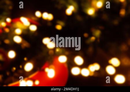 Bright, blurry lights on a Christmas tree from a garland. Festive yellow bokeh out of focus on black background. Street decoration, macro concept. Cit Stock Photo