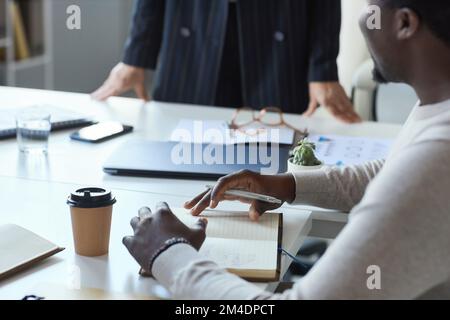 Close up of black man taking notes in planner during business meeting with team Stock Photo