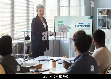 Portrait of senior businesswoman giving presentation in office while leading meeting with team, copy space Stock Photo