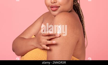 Closeup shot of black plus size lady rubbing moisturising lotion to skin on shoulder, enjoying body care, panorama Stock Photo