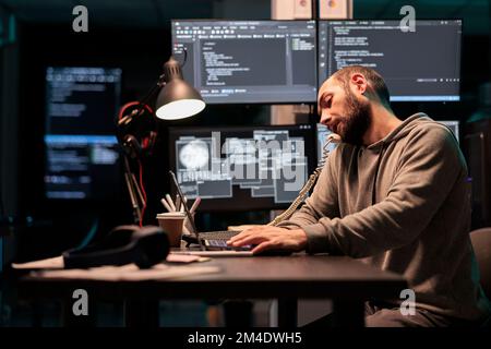 Software engineer talking on landline phone call after hours, answering office cord telephone to program code on terminal window. Database admin using phone line to develop new interface. Stock Photo