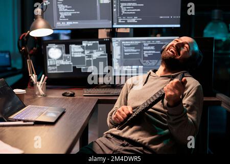 Cheerful programmer singing at air guitar keyboard late at night, working on cloud computing html script. Having fun with artificial intelligence and data on terminal window, fooling around. Stock Photo