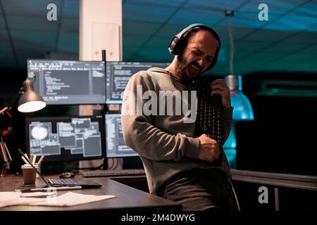 Male software engineer playing guitar with keyboard, writing code with cloud computing and programming html source. Cheerful smiling developer having fun and acting silly in office. Stock Photo