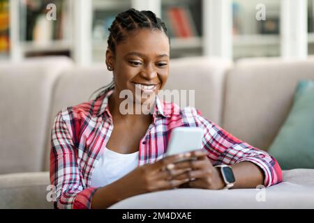 Cheerful beautiful black woman using smartphone at home Stock Photo