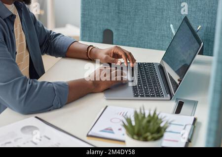 Close up of unrecognizable black man typing at laptop keyboard while using laptop at workplace, copy space Stock Photo