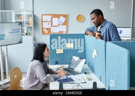 Side view at two young colleagues talking over cubicle wall in office, copy space Stock Photo