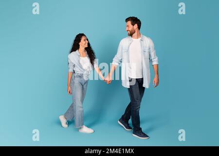 Cheerful handsome young european bearded guy leads the hand of lady in casual, isolated on blue background Stock Photo