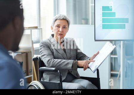 Portrait of senior woman using wheelchair while giving presentation in business meeting Stock Photo