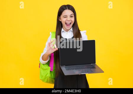 Funny face. School girl hold laptop notebook on isolated studio background. Schooling and education concept. Screen of laptop computer with copy space Stock Photo