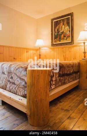 Rustic four poster bed in small upstairs guest bedroom with nuanced brown stained floorboards inside log home. Stock Photo