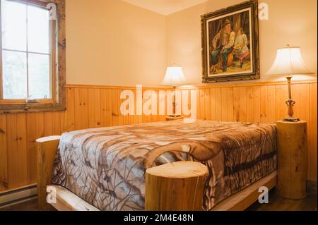 Rustic four poster bed in small upstairs guest bedroom with nuanced brown stained floorboards inside log home. Stock Photo