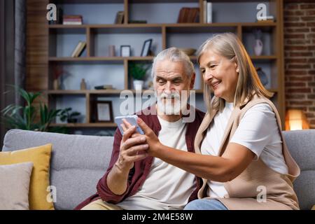 Mature happy couple communicates online call. A gray-haired husband and wife are talking to relatives on the phone. Video call on smartphone. Remote Stock Photo