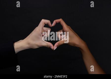 Two people belonging to different races making a heart with their hands Stock Photo