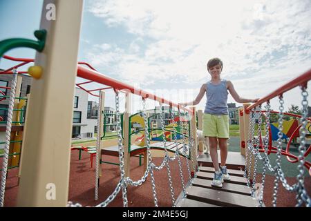 Full length portrait of young boy playing on colorful playground and walking towards camera across bridge, copy space Stock Photo